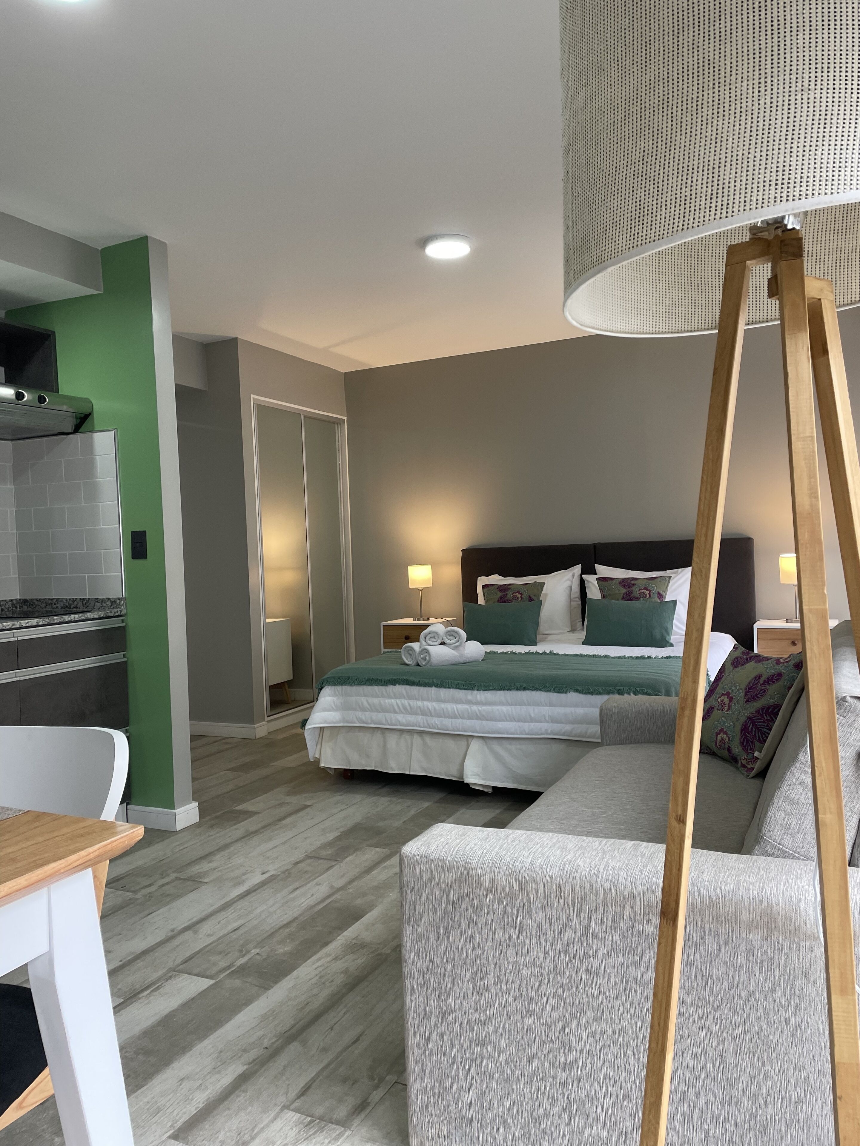 A modern hotel room with a bed, a sofa, a dining table, and a kitchenette.