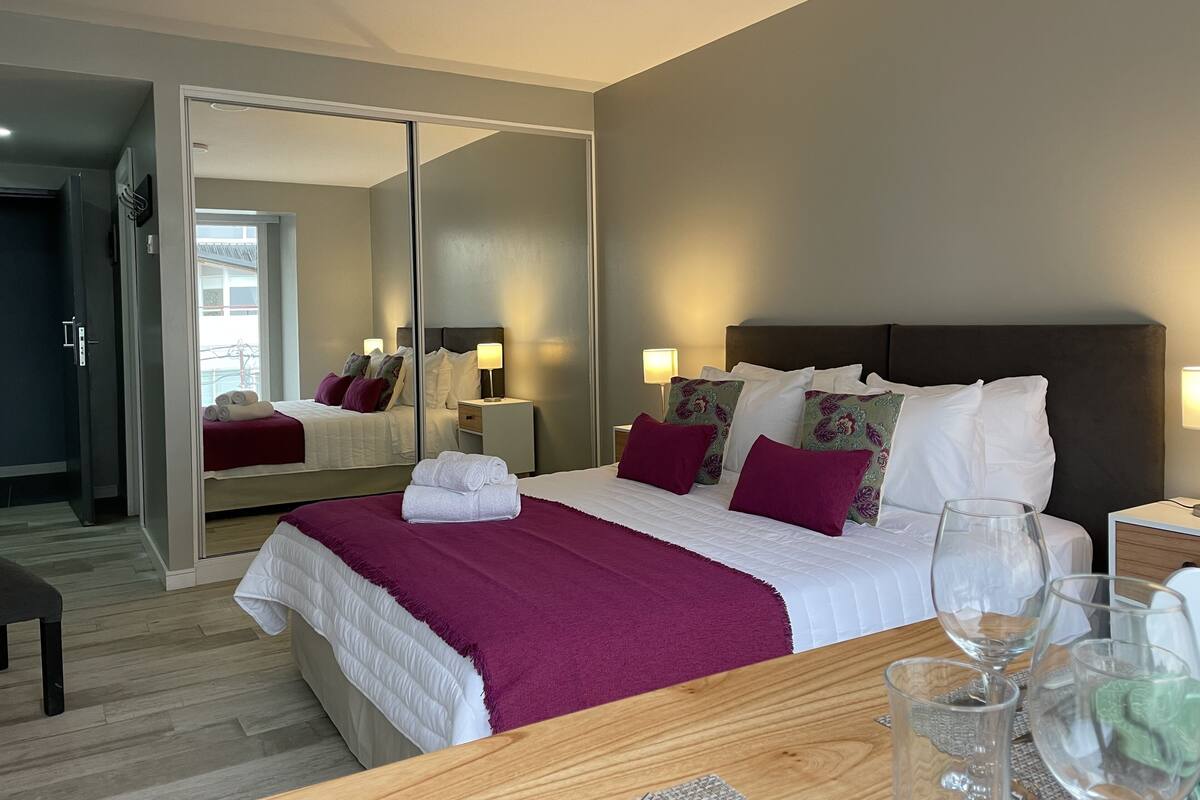 Une chambre d’hôtel moderne avec un grand lit, une table de chevet en bois et une table en verre avec des verres à vin.
