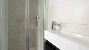 Un bagno moderno con cabina doccia in vetro, lavabo bianco e rubinetteria cromata.