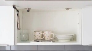 Un pensile da cucina con un bicchiere, due tazze e un piatto.