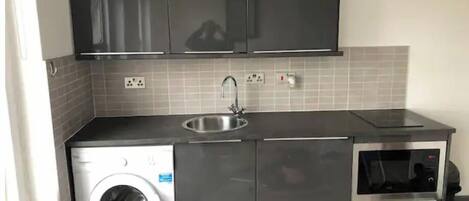 A compact kitchen with a washing machine, a sink, and a microwave.