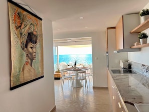 Una cocina moderna con vistas al mar, un comedor con sillas blancas y un cuadro grande en la pared.