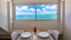A dining table with plates, glasses, and cutlery, set against a window with a view of the sea and sky.