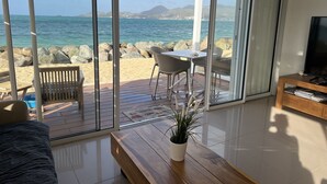A modern living room with a large sliding glass door leading to a deck with a view of the ocean and rocky shoreline.