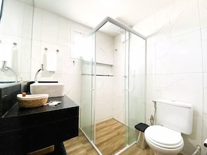 A modern bathroom with a glass-enclosed shower, a black countertop, a white sink, and a toilet.