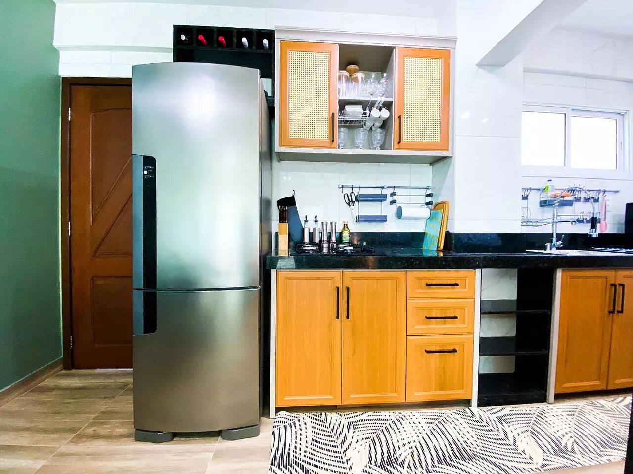 Una cocina con refrigerador de acero inoxidable, armarios de madera y encimera negra.