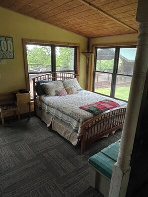 A bedroom with a wooden bed, a nightstand, a bench, and large windows.