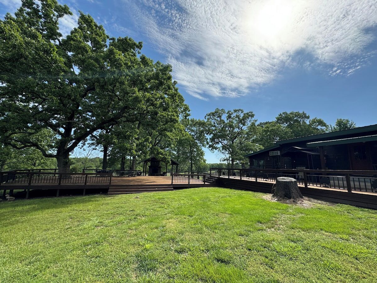 A park with a large tree, a gazebo, and a covered area with a railing.