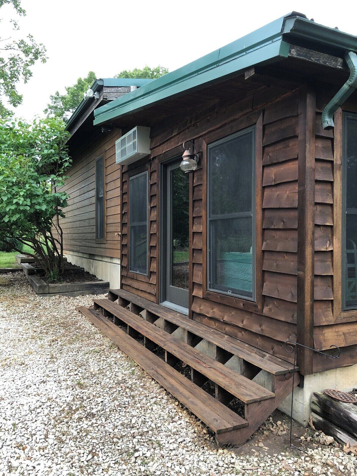 A wooden cabin with a gravel driveway and a wooden deck.