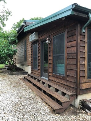 A wooden cabin with a gravel driveway and a wooden deck.