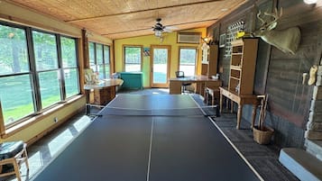 Een tafeltennistafel in een kamer met houten wanden en een plafondventilator.
