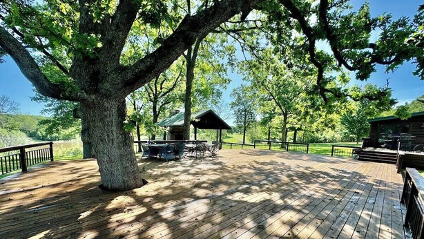 A wooden deck with a picnic table and chairs, surrounded by trees.