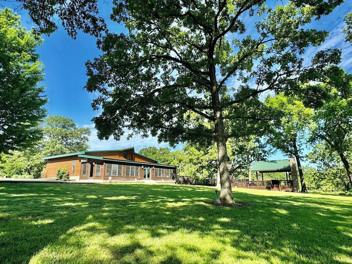 A building with a brick exterior and a green roof, surrounded by a well-maintained lawn and trees.