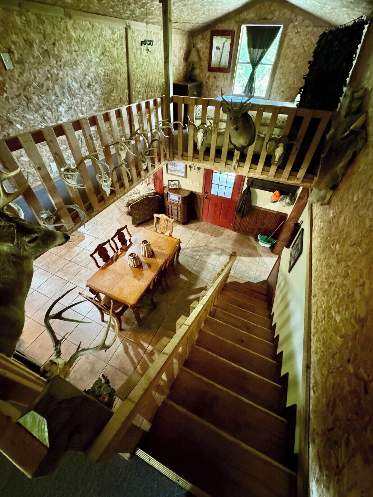 A rustic interior with a wooden staircase, a dining area with a table and chairs, and a loft space with a wooden railing.
