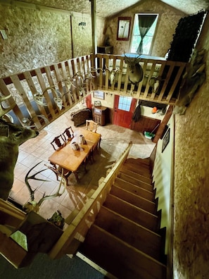 Ein rustikales Interieur mit einer Holztreppe, einem Essbereich mit Tisch und Stühlen sowie einem Schlafbereich mit Holzbalkon.