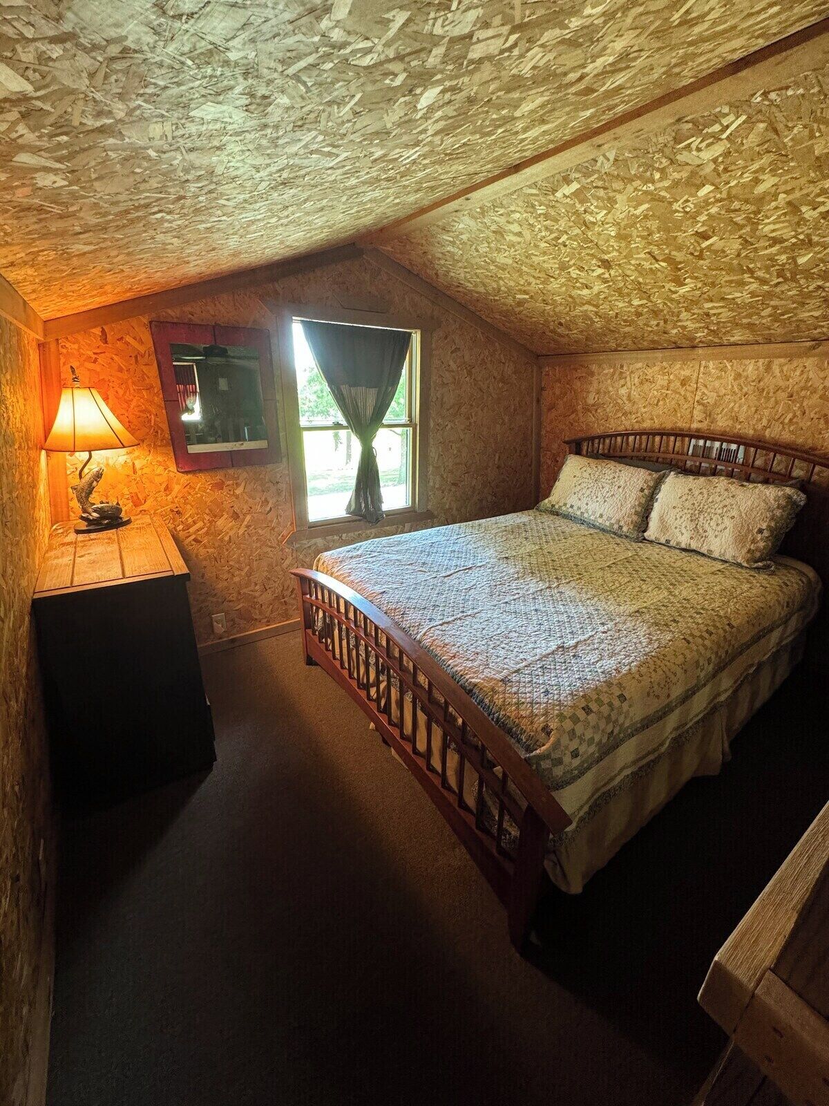 A bedroom with a wooden bed, a nightstand, a lamp, and a window with curtains.