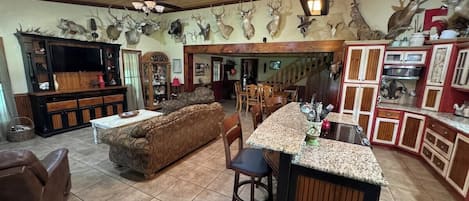 A spacious living area with a large sofa, a bar area with a granite countertop, and a dining area with wooden furniture.