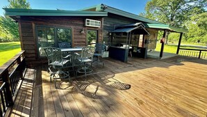 A wooden deck with outdoor furniture, a covered area, and a view of a green landscape.
