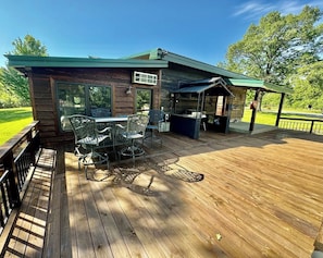 A wooden deck with outdoor furniture, a covered area, and a view of a green landscape. - Seven Oaks sleeps 8, outdoor adventures (Quapaw)
