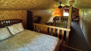 A bedroom with a wooden ceiling, a bed with patterned bedding, a wooden bench, and a lamp.
