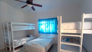 Un dormitorio con literas, un ventilador de techo y una ventana con cortinas azules.