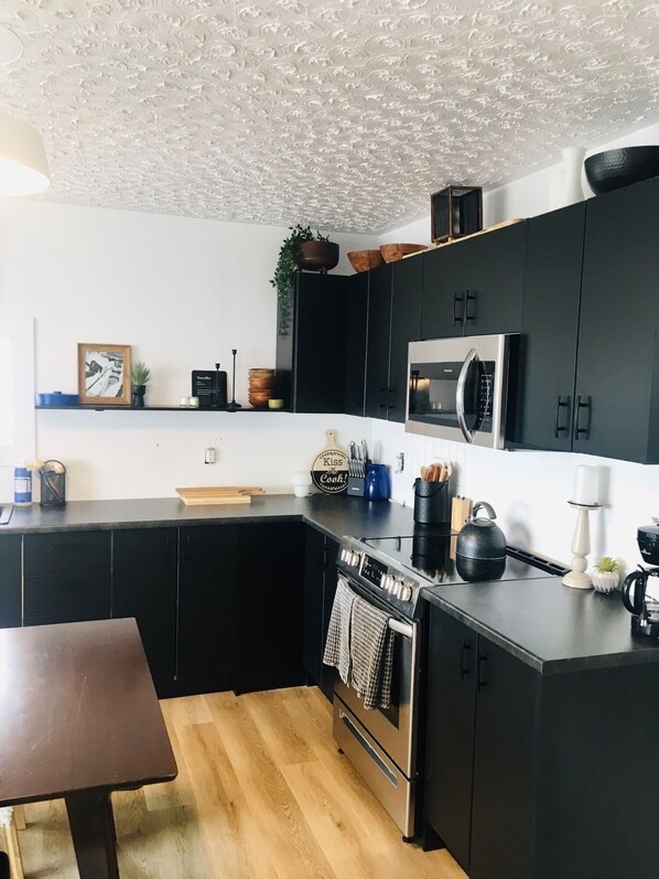 A modern kitchen with black cabinets, a stainless steel oven, a microwave, and a wooden dining table. - The Camp House (Turkey Point)