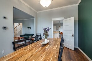 A dining area with a wooden table, chairs, and a vase of flowers. There is a staircase in the background leading to another room. - Family Escape ✓PETS OK Game Room Fenced Backyard (Plano)