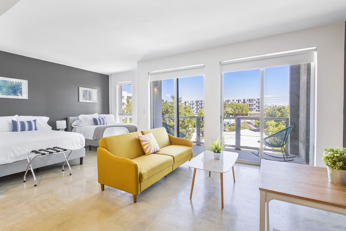 A modern hotel room with a bed, sofa, and balcony with a view.
