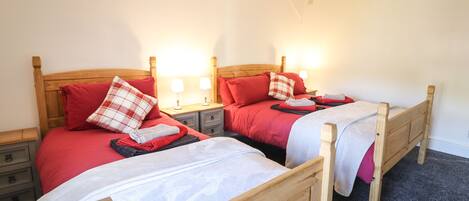 Two wooden beds with red bedding and white headboards, each with a nightstand and a lamp.