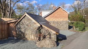 A stone building with a sloped roof and a wooden wheel. - Tan Y Capel (Llanbrynmair)
