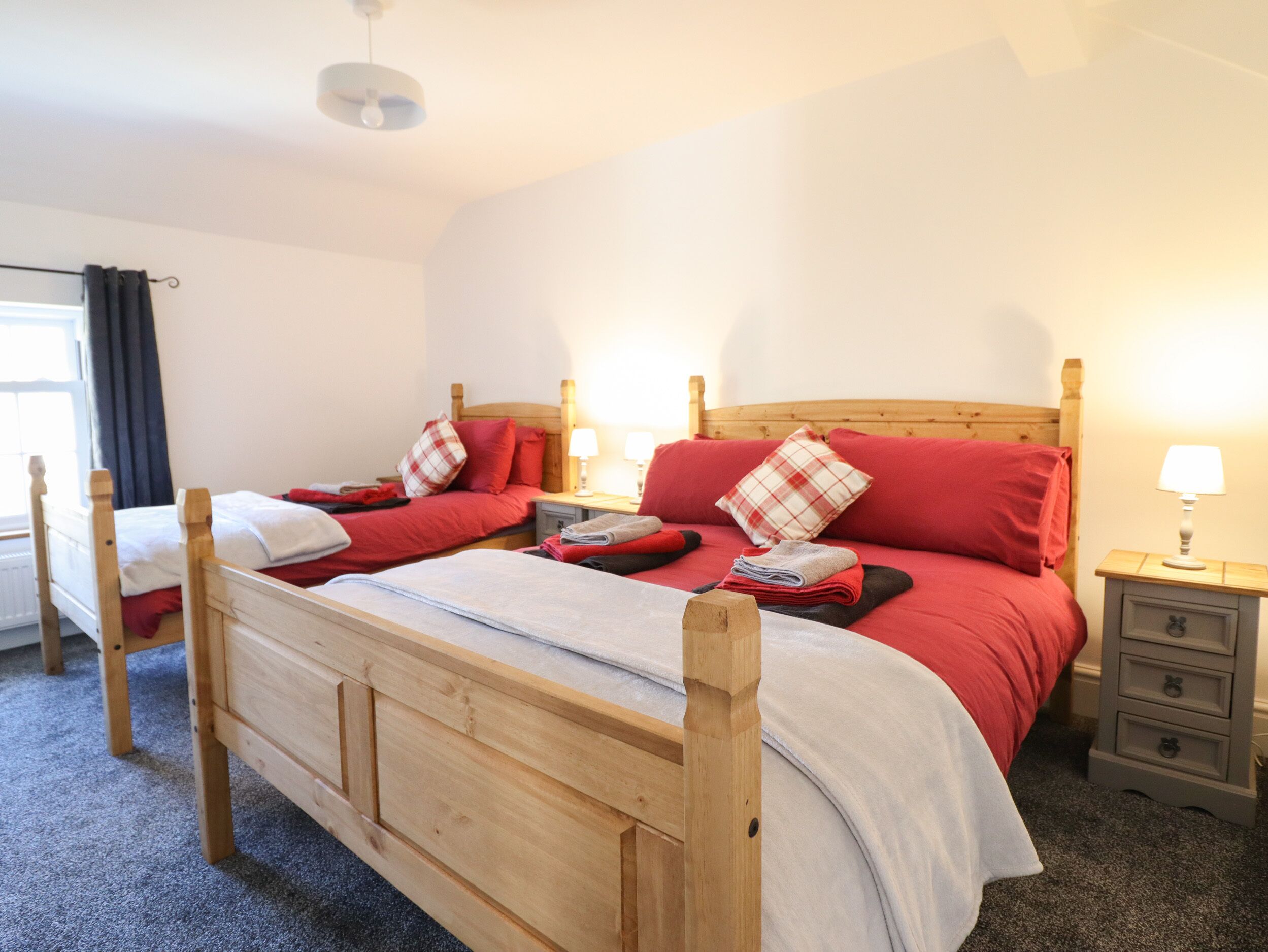 Ein Doppelbett mit Holzrahmen, zwei Nachttische, ein Fenster mit Vorhängen.