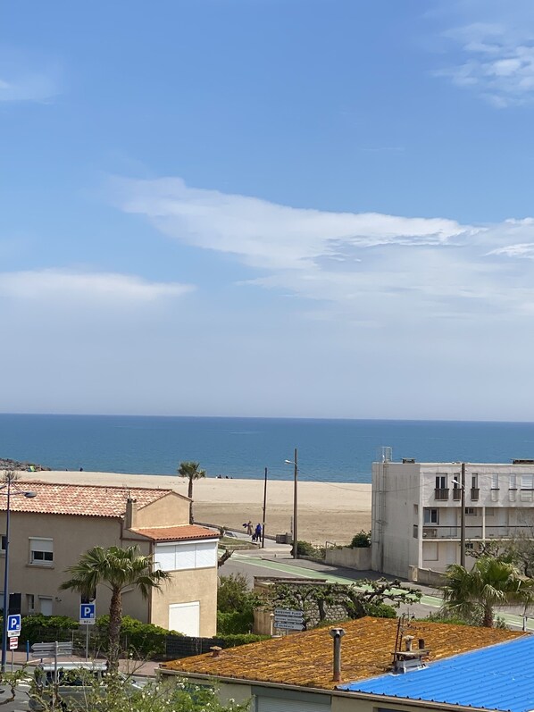 A coastal view with a beach, a parking area, and buildings with balconies.