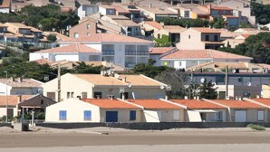A coastal residential area with houses featuring red-tiled roofs and a sandy beach in the foreground. - Cosy T3 100m from the beach in a recent residence. (Fleury D'aude)