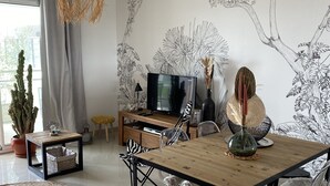 A modern living room with a wooden dining table, clear chairs, a TV, and decorative wall art. - Cosy T3 100m from the beach in a recent residence. (Fleury D'aude)