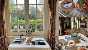 Uma área de refeições com uma mesa posta para dois, uma janela com vista para vegetação e um candelabro decorativo.