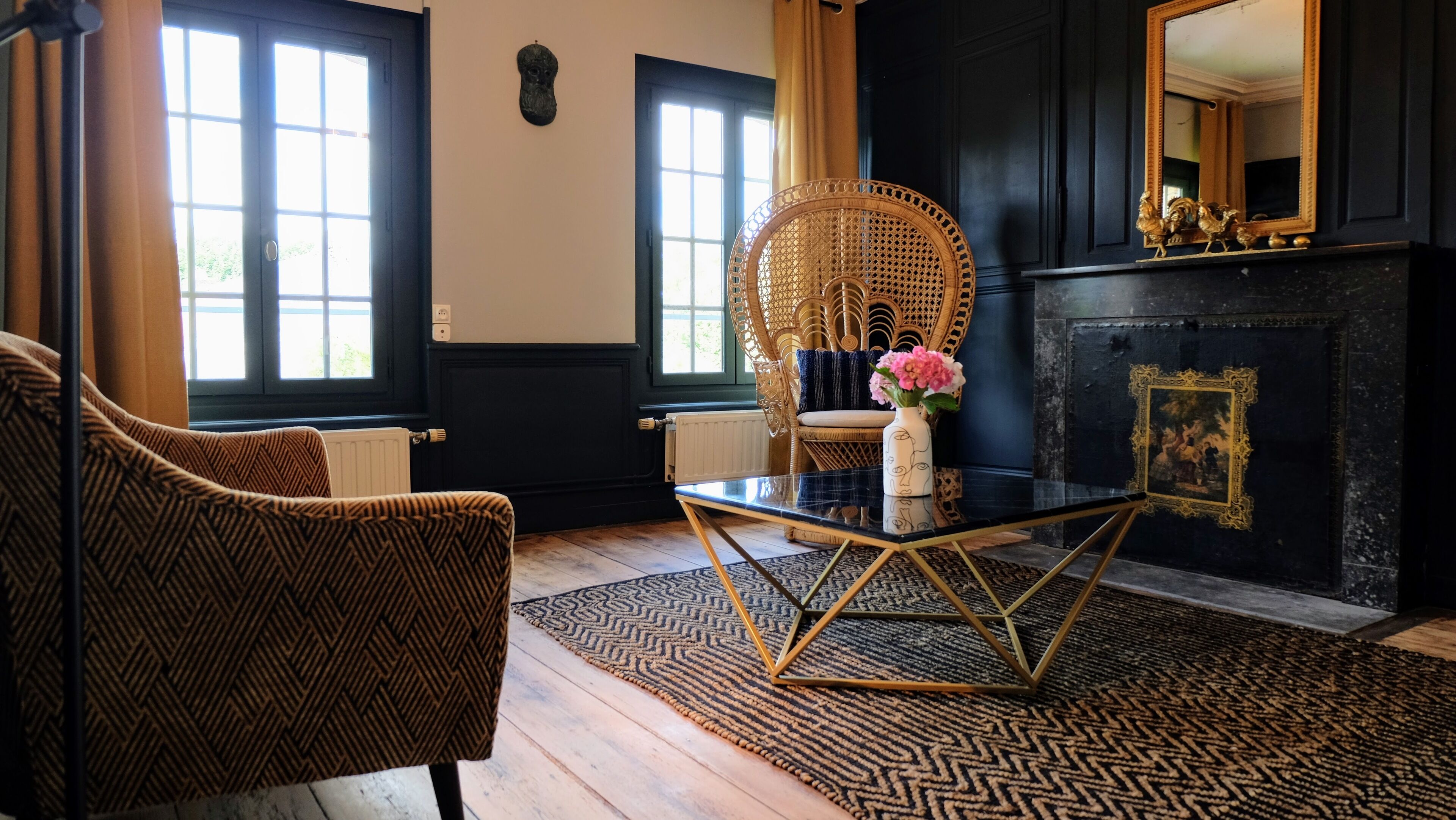 Une pièce dotée d'une grande fenêtre, d'un fauteuil en osier, d'une table basse en verre et d'une cheminée.