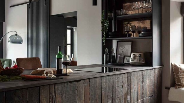 A modern kitchen with a rustic wooden island, black pendant lights, and a built-in wine rack.