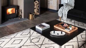 A cozy living room with a stone wall, a fireplace, a black sofa, and a patterned rug.