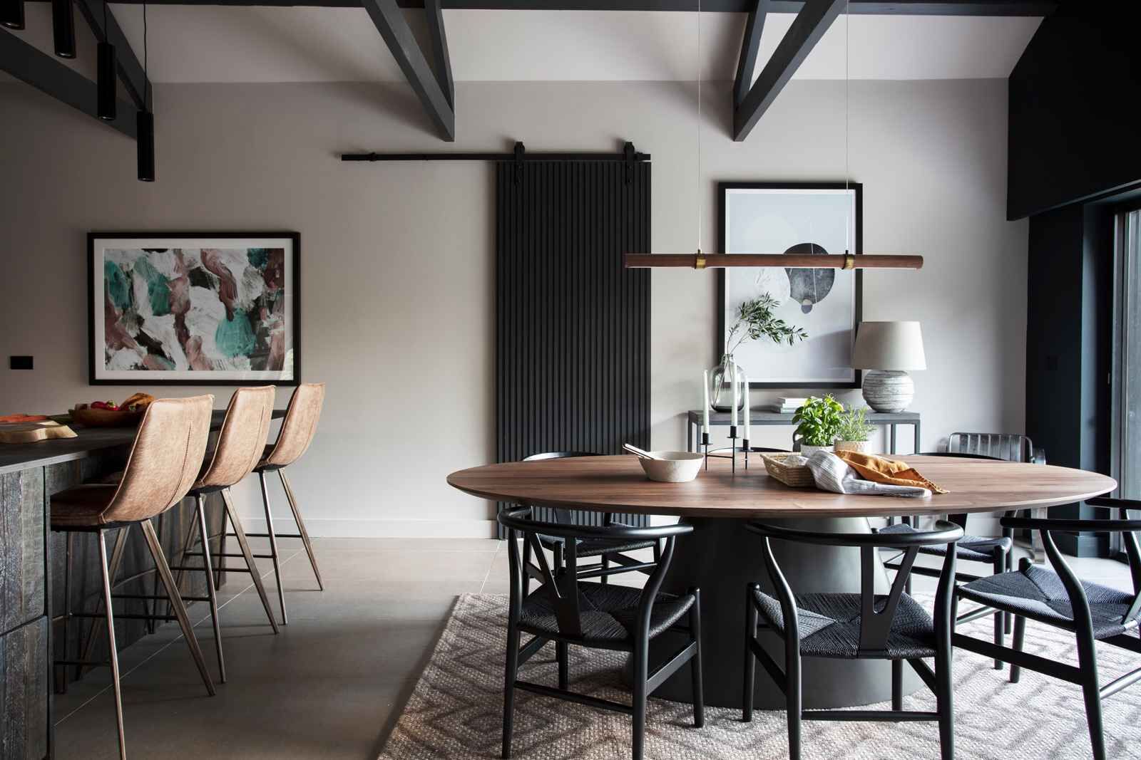 Een moderne eethoek met een ronde houten tafel, zwarte stoelen en een bar met krukken.