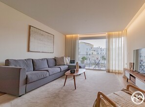 Un salon moderne avec un canapé gris, une petite table basse ronde et un téléviseur posé sur un meuble en bois.