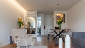 Un salon moderne avec un coin repas, comprenant un canapé, une table basse et une table à manger avec des chaises. On y trouve également des vases décoratifs et un luminaire suspendu.