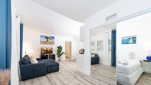 Un salon moderne comprenant un canapé, un coin repas et un mur miroitant qui reflète un lit.