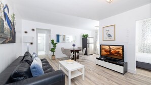 Un salon moderne avec un canapé en cuir noir, une table basse blanche, un téléviseur et un coin repas comprenant une table et des chaises.