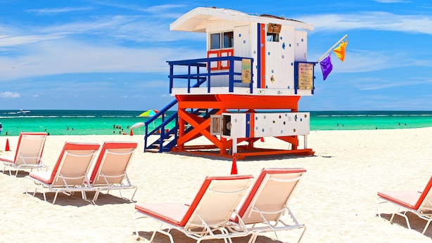 Une tour de surveillance avec un drapeau, des chaises de plage et une vue dégagée sur l’océan.