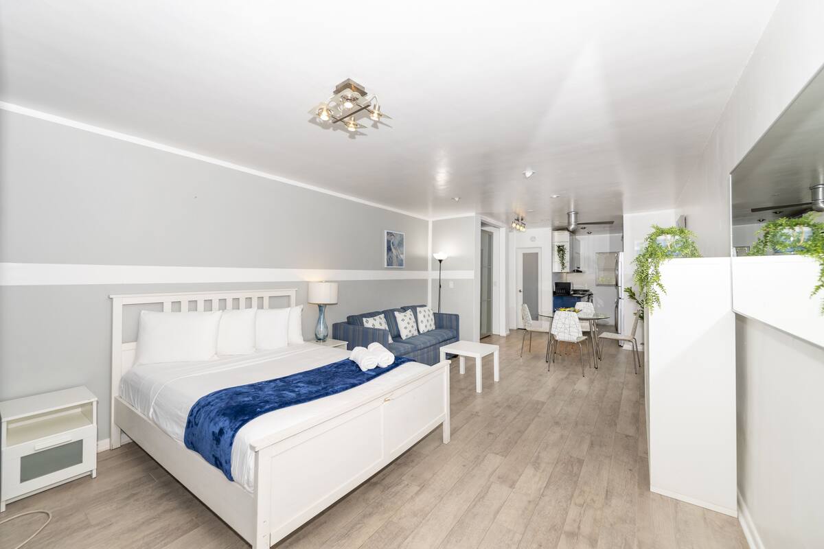 Et moderne soveværelse med en hvid seng, et blåt plaide, et lille hvidt bord og en blå sofa.
