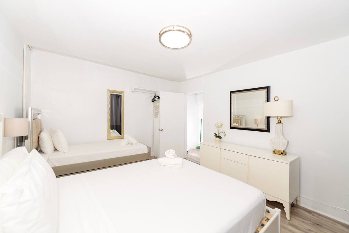 Et hotelværelse med en stor seng, et natbord med lampe, et kommode og et spejl.