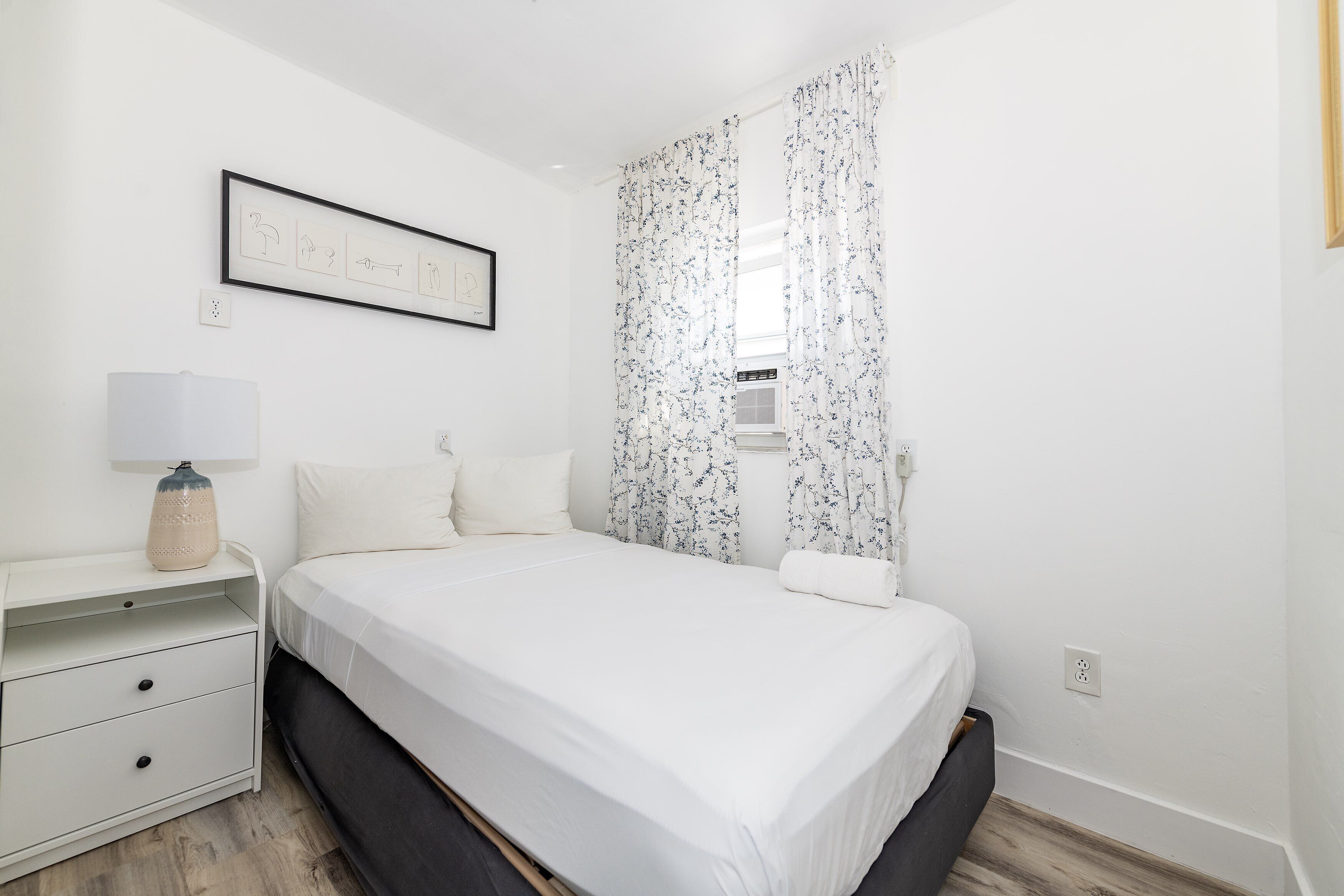 A bedroom with a bed, a nightstand, a lamp, and a framed picture on the wall.