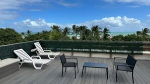 A rooftop terrace with lounge chairs and a table, overlooking a beach with palm trees and the ocean. - OCEAN DRIVE APARTMENTS (Miami Beach)