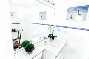 Une salle de bain moderne avec un lavabo blanc, un miroir et une étagère contenant des articles de toilette.