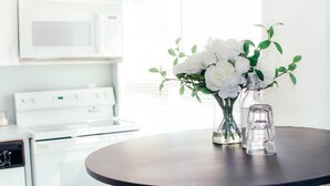 A kitchen with white appliances, a round table with a vase of flowers, and a clear glass. - OCEAN DRIVE APARTMENTS (Miami Beach)